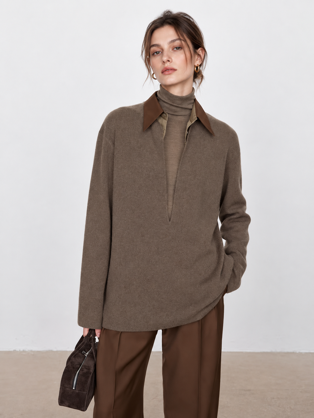 Model in a taupe cashmere sweater with a detachable contrast collar, styled with a tonal turtleneck and chocolate brown trousers.”